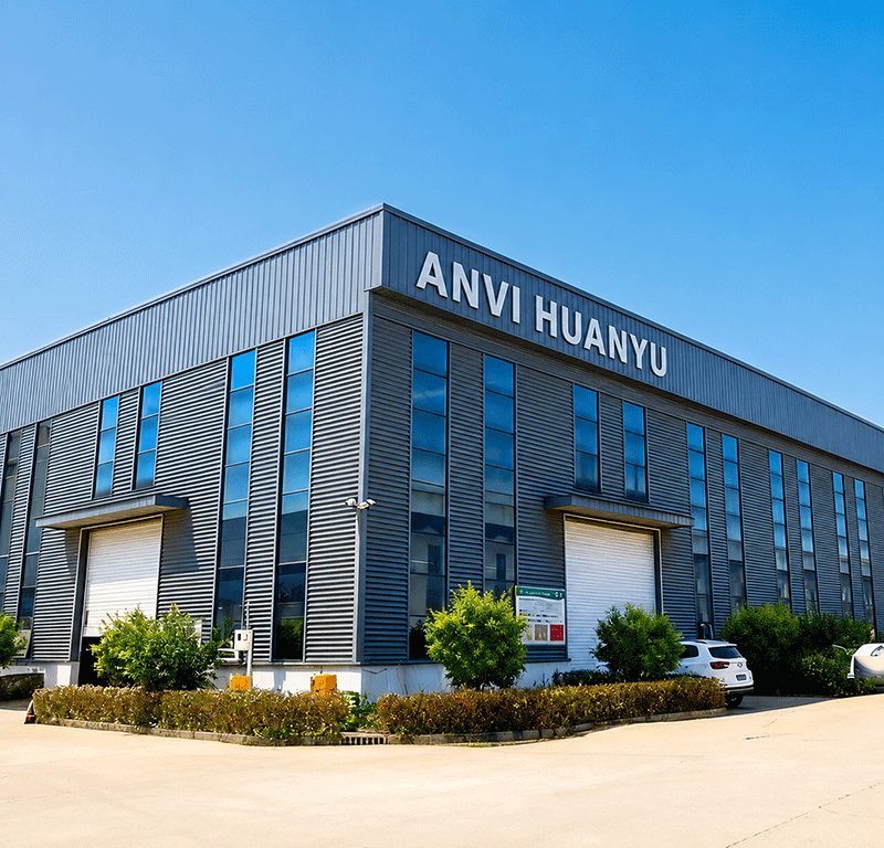 Modern industrial factory building with grey metal facade prominently displaying "ANVI HUANYU" signage, surrounded by neat landscaping under a clear blue sky. Professional manufacturing facility for HDPE ground protection mats.