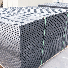 Neatly stacked black HDPE ground protection mats with diamond tread, securely strapped on a pallet in the factory