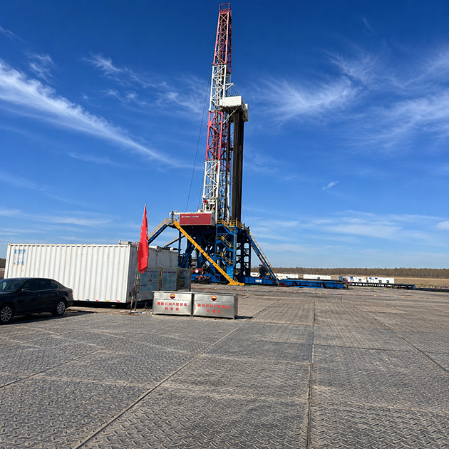 Products Heavy-duty composite rig mats layered on an oilfield drilling site under a blue sky, showcasing ground protection and temporary roadway solutions for drilling rigs.